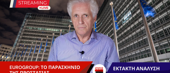 Ο Παναγιώτης Αποστόλου μιλά σε έκτακτη ανάλυση για το Eurogroup, με φόντο το κτίριο της Ευρωπαϊκής Επιτροπής στις Βρυξέλλες και σημαίες της Ευρωπαϊκής Ένωσης.